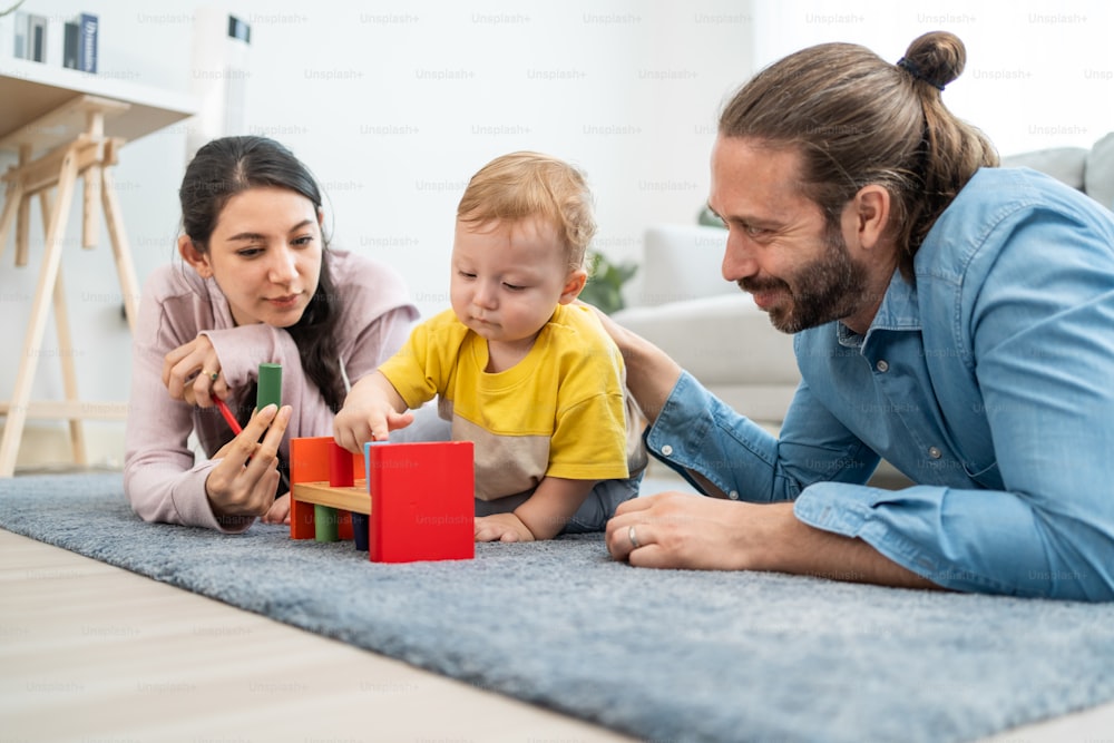 Caucasian happy loving parent play with baby toddler in living room. Attractive couple mother and father spend time with young little infant son child in house. Activity relationship at home concept.