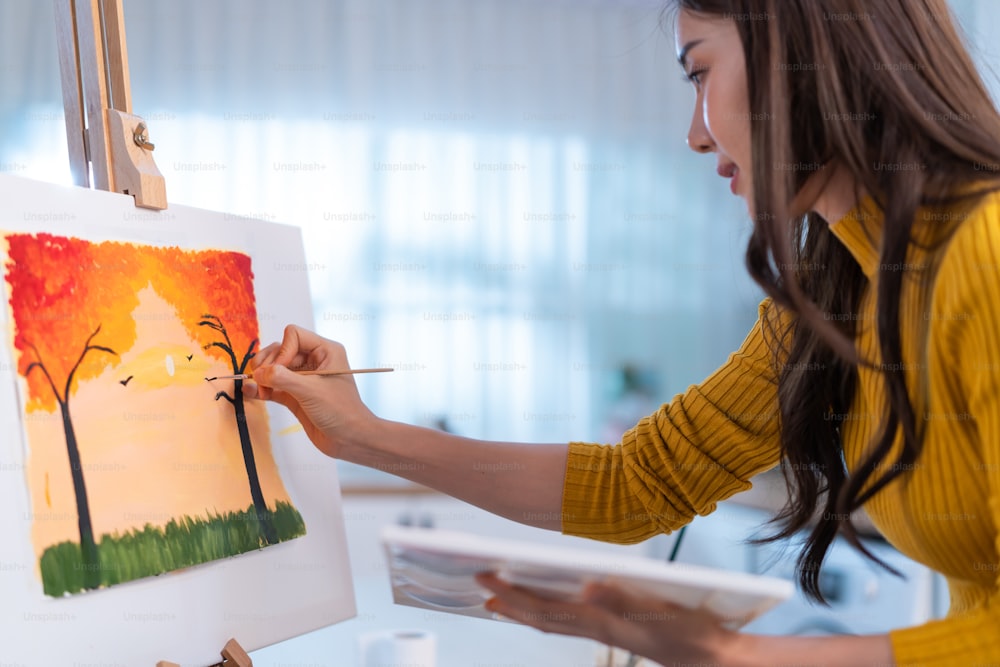 Joven artista asiática talentosa que colorea en tablero de pintura en casa. Atractiva hermosa imagen femenina dibuja, creando obras de arte con pintura de acuarela y pincel disfruta de la actividad de la creatividad en casa.