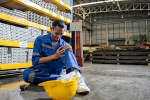 Asian industrial worker suffer from leg pain while work in manufactory. Attractive young handsome male industry factory engineer having an accident and massage knee at warehouse manufacturing plant.