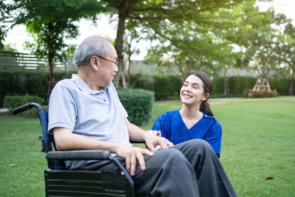 Caucasian Caregiver doctor talk with older disabled man on wheelchair. Attractive nurse taking care of senior elderly mature male handicapped patient at green park. Medical insurance service concept.