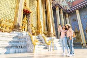 Feliz viajera asiática amiga con cámara haciendo turismo en el templo del Buda de Esmeralda, Wat Phra Kaew, popular lugar turístico en Bangkok, Tailandia