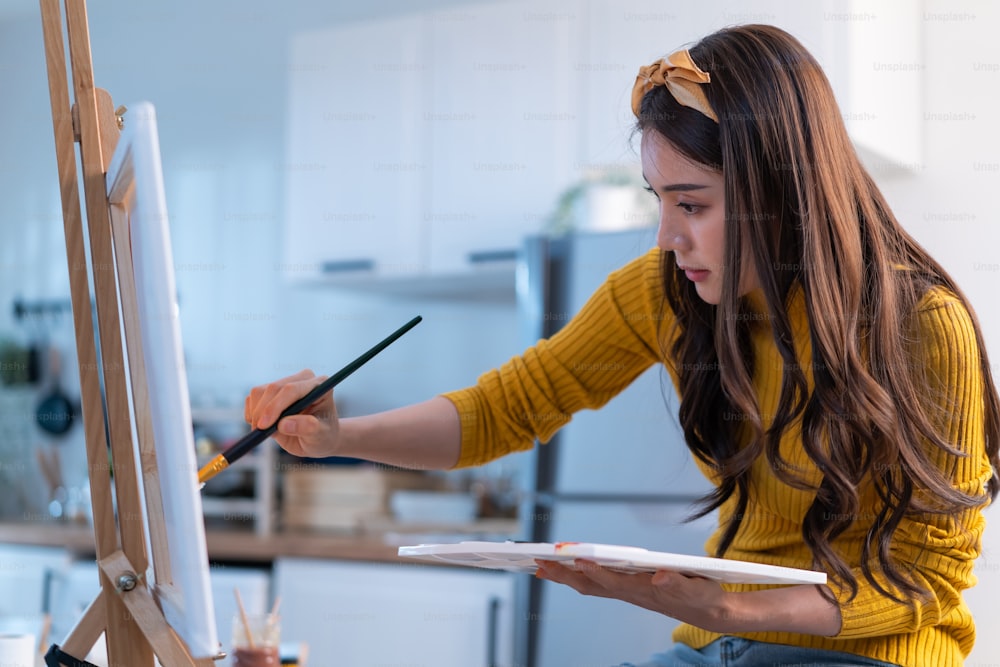 Jeune femme talentueuse asiatique artiste coloriage sur tableau de peinture dans la maison. Belle image d’art de dessin féminine attrayante, créant des œuvres d’art avec de la peinture à l’aquarelle et un pinceau, profitez d’une activité de créativité à la maison.