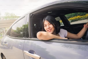 Mujer asiática sonriente feliz conduciendo su nuevo coche con confianza