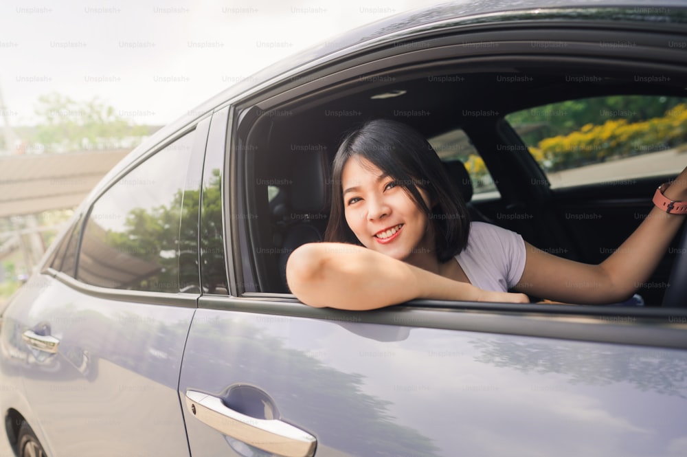 Donna asiatica sorridente felice che guida la sua nuova auto con fiducia