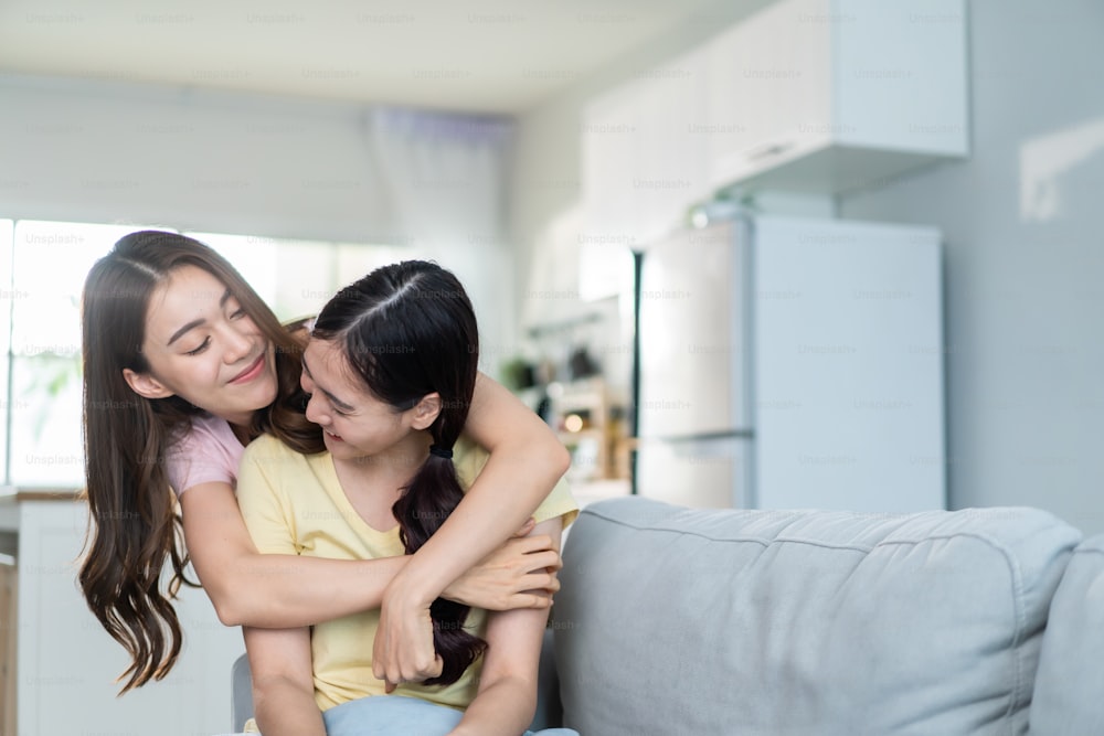 Asiatische schöne lesbische Frauen Paar umarmt Freundin im Wohnzimmer. Attraktive zwei schwule Freundinnen, die auf dem Sofa im Wohnzimmer sitzen, sich glücklich fühlen und die Zeit miteinander im Urlaub im Haus verbringen