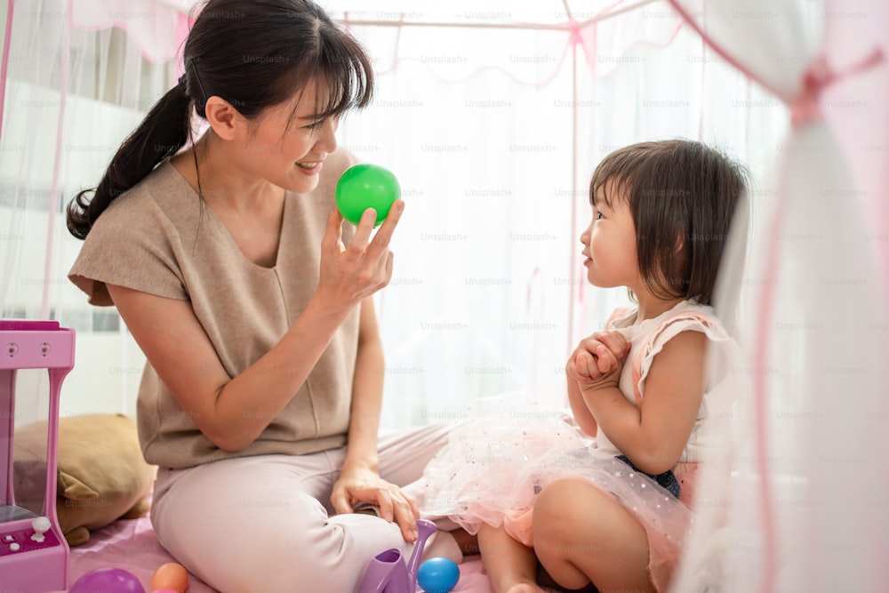 Asiatische schöne liebevolle Mutter unterrichten junge kleine Mädchen Tochter über Farbe im Zelt zu Hause. Eltern spielen Bildungsspiel mit Kind, um Sprechfähigkeiten zu lernen und zu entwickeln. Erziehungsaktivität im Hauskonzept