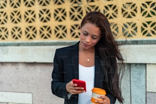 Junge Frau steht auf der Straße, trinkt Kaffee und benutzt ein Smartphone. Mädchen surft im Internet, chattet, bloggt. Frau hält das Telefon und schaut auf ihren Bildschirm.
