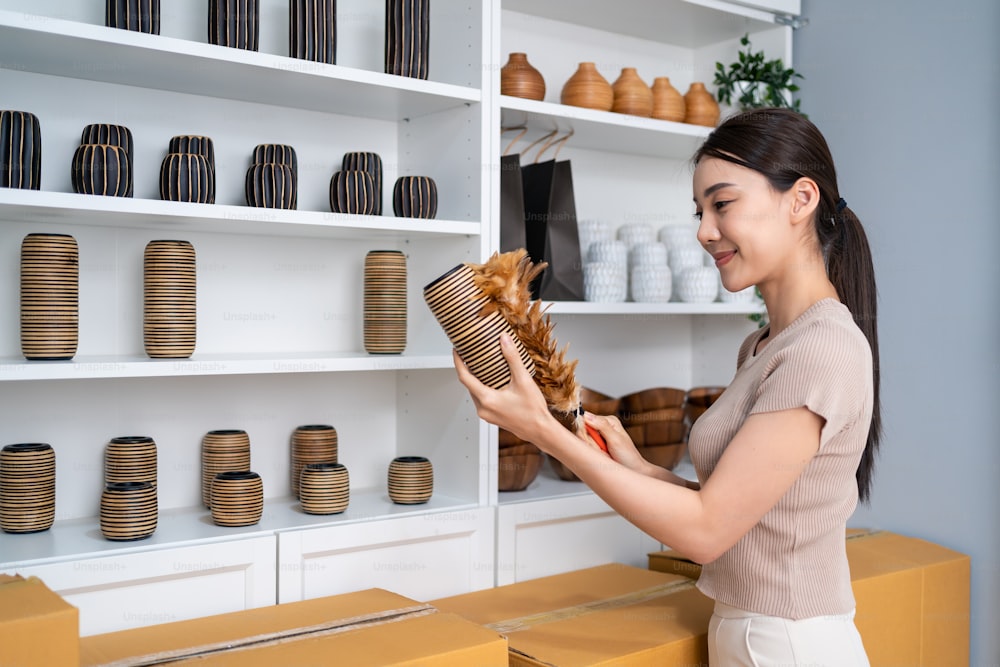 Asian beautiful woman clean vase goods order for customer from shelf. Young attractive business girl working to preparing parcel boxes checking ecommerce shipping online retail to sell at home store.