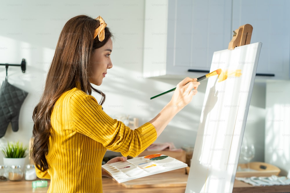 Joven artista asiática talentosa que colorea en tablero de pintura en casa. Atractiva hermosa imagen femenina dibuja, creando obras de arte con pintura de acuarela y pincel disfruta de la actividad de la creatividad en casa.