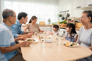 Asian big happy family have lunch on eating table together in house. Senior elder grandparent, young couple and little kid daughters feel happy, enjoying food in house. Activity relationship concept.