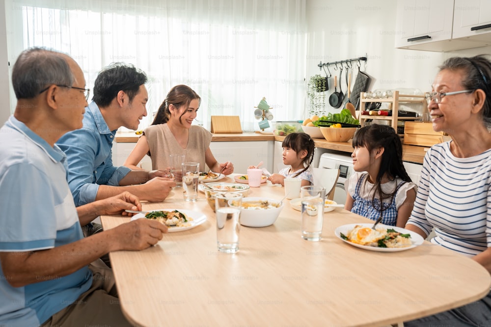 Asian big happy family have lunch on eating table together in house. Senior elder grandparent, young couple and little kid daughters feel happy, enjoying food in house. Activity relationship concept.