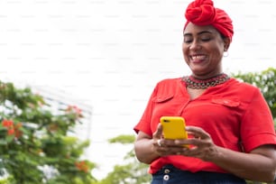 Happy trendy Afro woman using smartphone and smiling on park