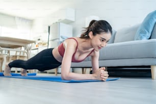 Asian Beautiful young woman stay home, doing cardio exercise at home. Attractive girl doing lockdown activity workout by plank on floor follow instruction video from online trainer for health in house