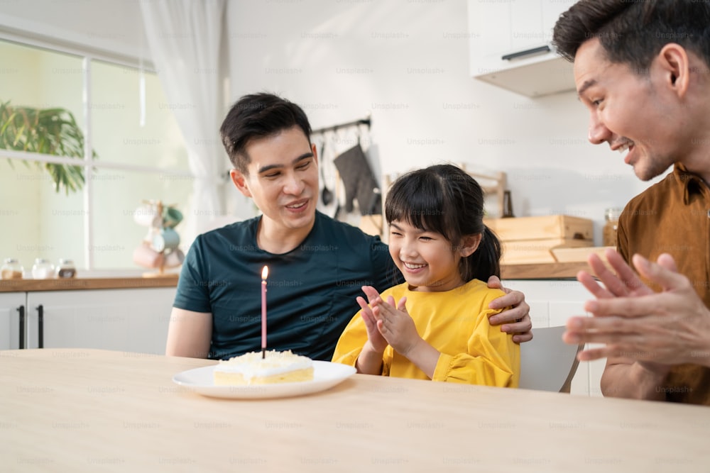 Asian attractive happy family celebrate birthday for girl kid in house. Handsome male take care and surprise little adorable adopt child daughter with cake and present gift on her special day at home.