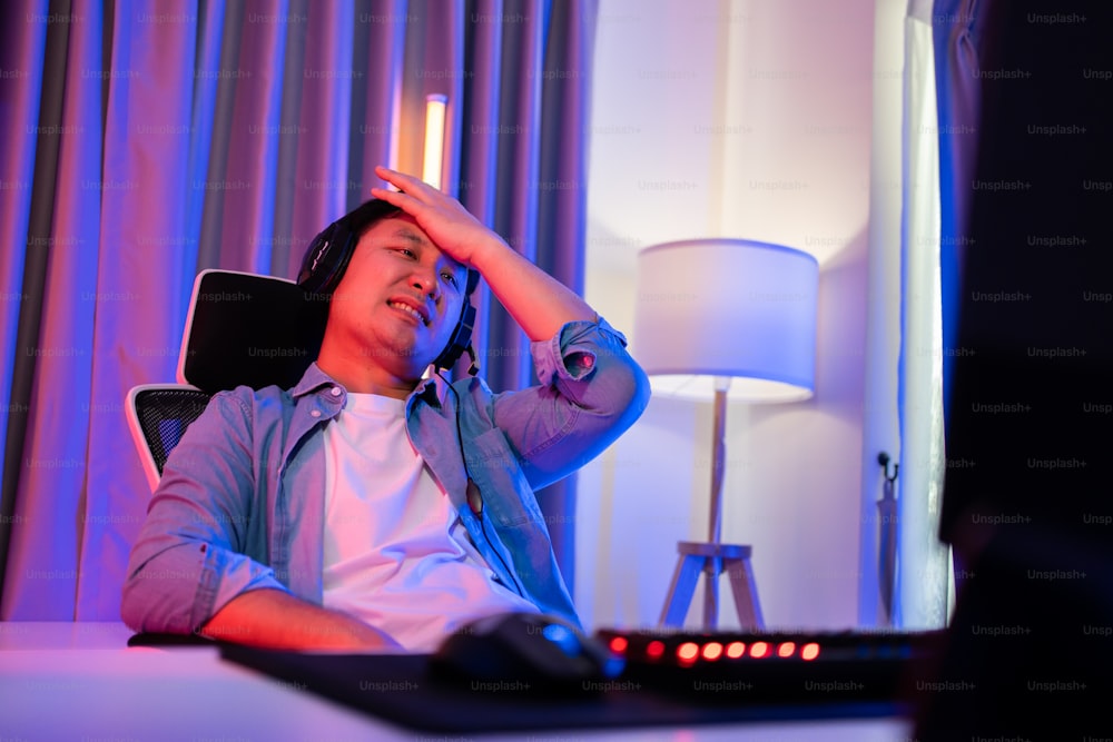 Un joueur masculin asiatique attrayant d’Esport joue à un jeu vidéo en ligne sur ordinateur. Un joueur perdant de jeu d’un bel homme contrarié se sent frustré et en colère lors de la diffusion en direct d’un cybertournoi à la maison.
