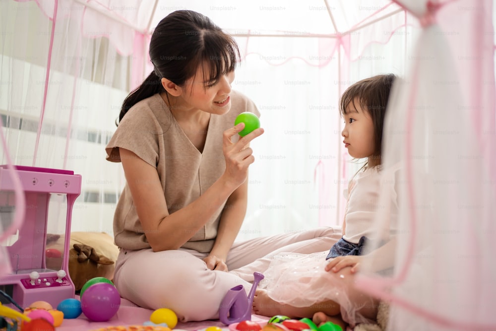 La madre asiática enseña a su hija sobre el color en la tienda de campaña en casa. Hermosos padres amorosos juegan un juego de educación con un niño pequeño para aprender y desarrollar habilidades para hablar. Concepto de actividad de crianza en casa