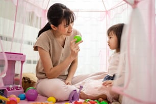 Asian mother teach young girl daughter about color in tent at home. Beautiful loving Parent play education game with little kid to learn and develop speaking skill. Parenting activity in house concept