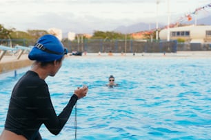 Personal trainer recording time on the stopwatch at the side of the pool during sports training