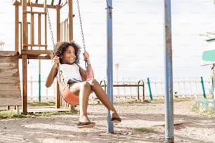 happy and smiling afro american girl playing on swing. fun and recreation concept.