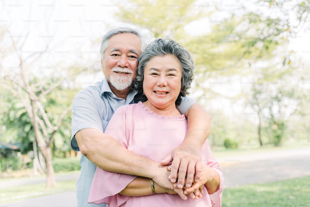Happy Asian senior couple smiling while holding each other outdoor in the park.