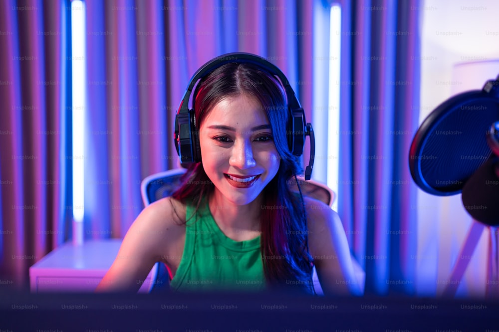 アジアの美しいeスポーツの女性ゲーマーは、コンピューターでオンラインビデオゲームをプレイします。魅力的な若い女の子のゲームプレーヤーは、自宅でサイバートーナメントをプレイしながら、幸せを感じ、テクノロジー放送のライブストリーミングを楽しんでいます