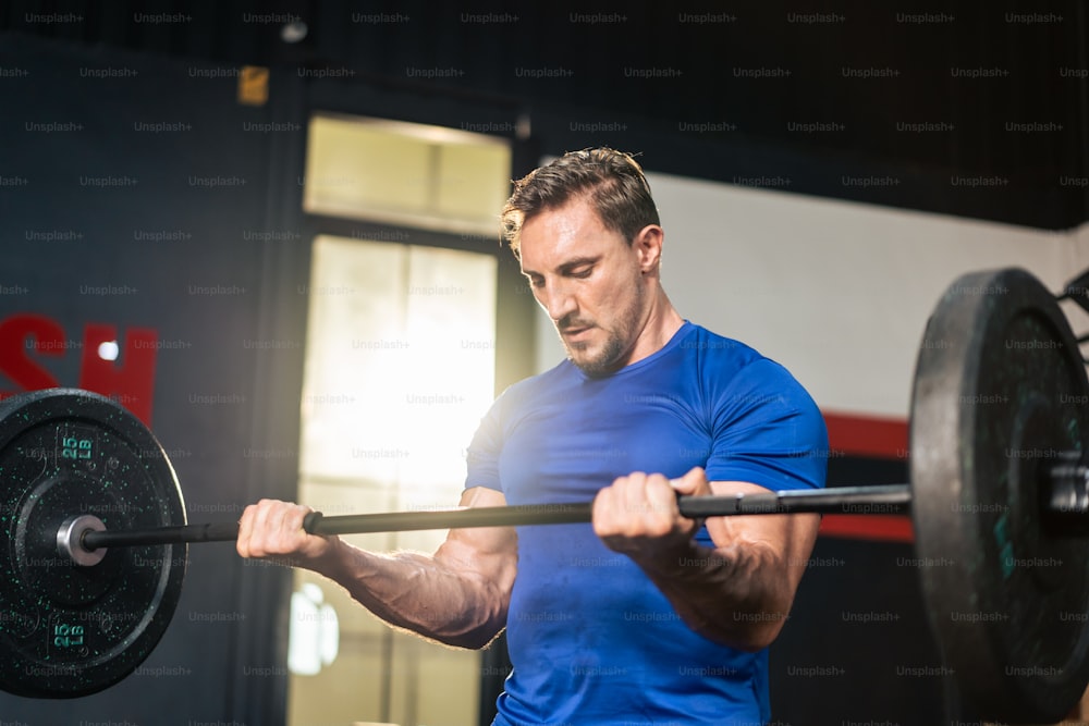 Caucasian sportsman slowly lift up weight machine barbell in stadium.  Active fitness trainer or athlete bodybuilder male working out, training exercise to maintain muscle for health care at gym club.