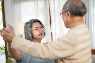 Asian happy Senior elderly Couple stay at home, spending leisure time in living room. Grandfather and grandmother enjoy retirement life and dancing together. Relationship and activity in house concept