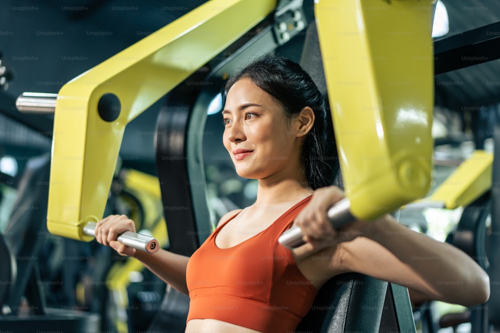 La deportista asiática levanta lentamente la máquina de pesas o la barra en el estadio. El ejercicio de entrenamiento femenino de atleta joven atractivo utiliza la herramienta del equipo de pesas para el cuidado de la salud y mantiene el músculo en el gimnasio.