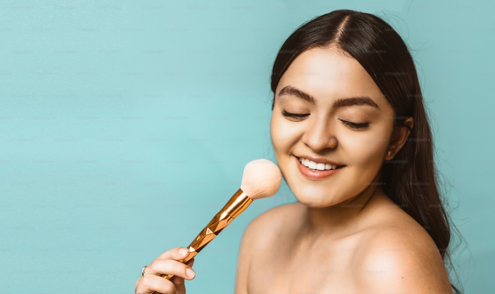 portrait of a young latinx woman holding a makeup brush. makeup and glamor concept.