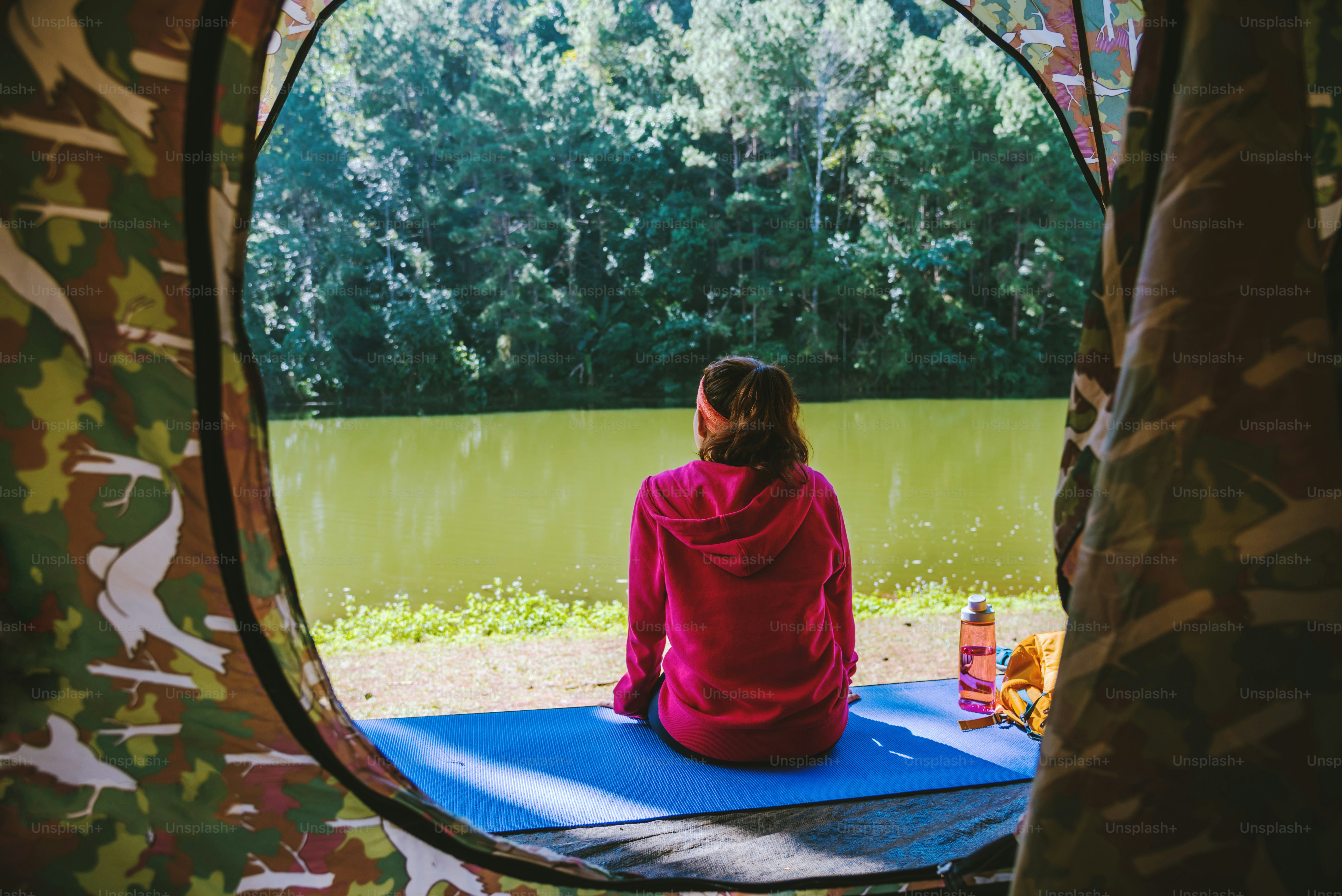 Young woman in the sport wear outfit is sitting and relaxing in the camping in the forest.
