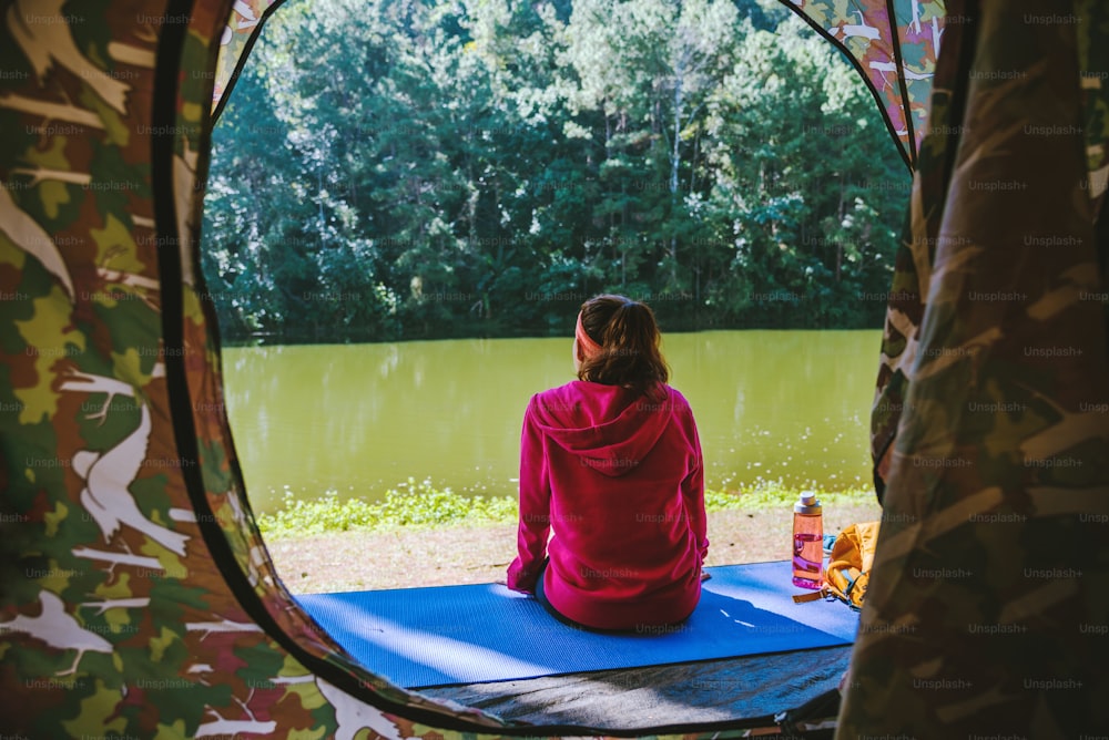 Junge Frau im Sportbekleidungs-Outfit sitzt und entspannt auf dem Campingplatz im Wald.