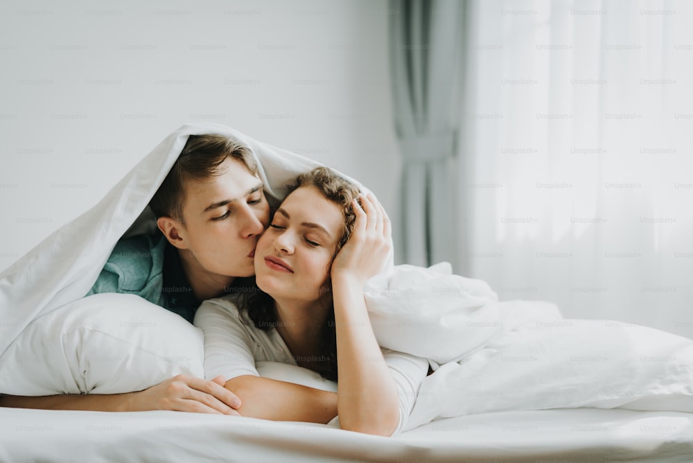 Glückliches junges, liebenswertes Paar küsst sich im Bett