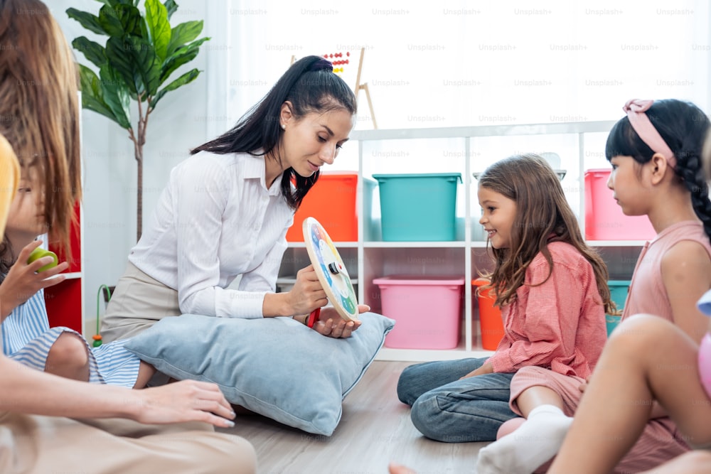 Kaukasische schöne junge Lehrerin, die Kindern in der Schule Kunst beibringt. Attraktive Lehrerin Meisterin erklärt und erzieht Zeichnen und Malen mit Schülerkindergarten Vorschule im Klassenzimmer.