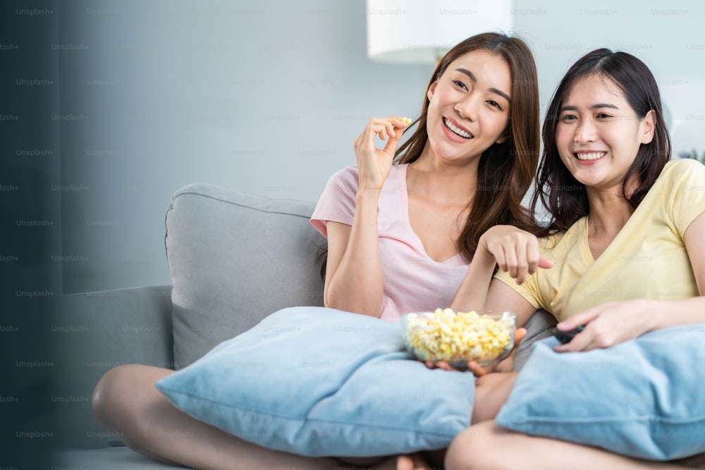 Asian beautiful lesbian woman couple enjoy watch TV together in house. Attractive two female gay friend sit on sofa in living room, feel happy watch movie on television. Homosexual-LGBTQ concept.