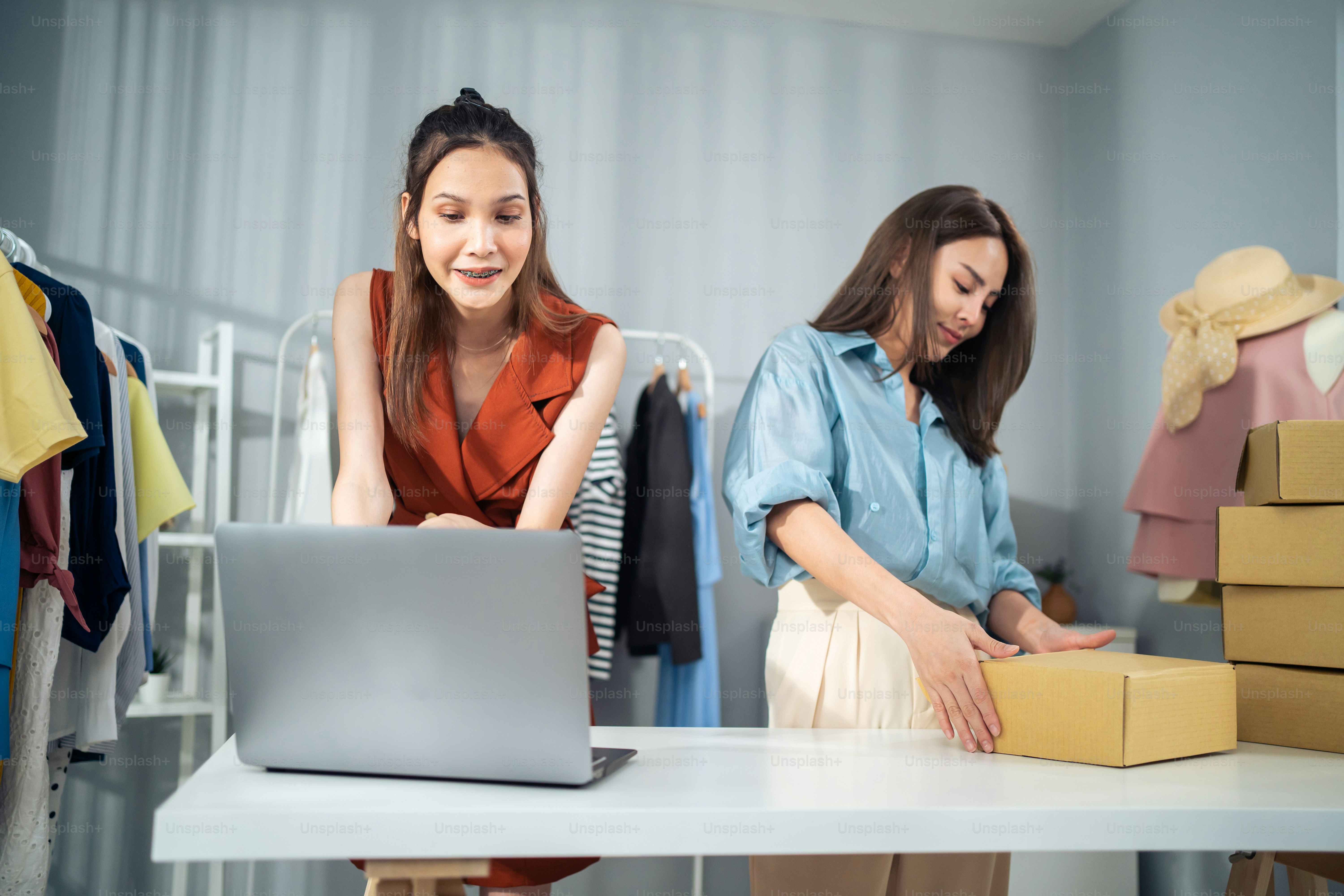 Asian woman friends couple packing clothes order into box for customer. Young attractive business people work to preparing parcel boxes check ecommerce shipping online retail to sell at office store.