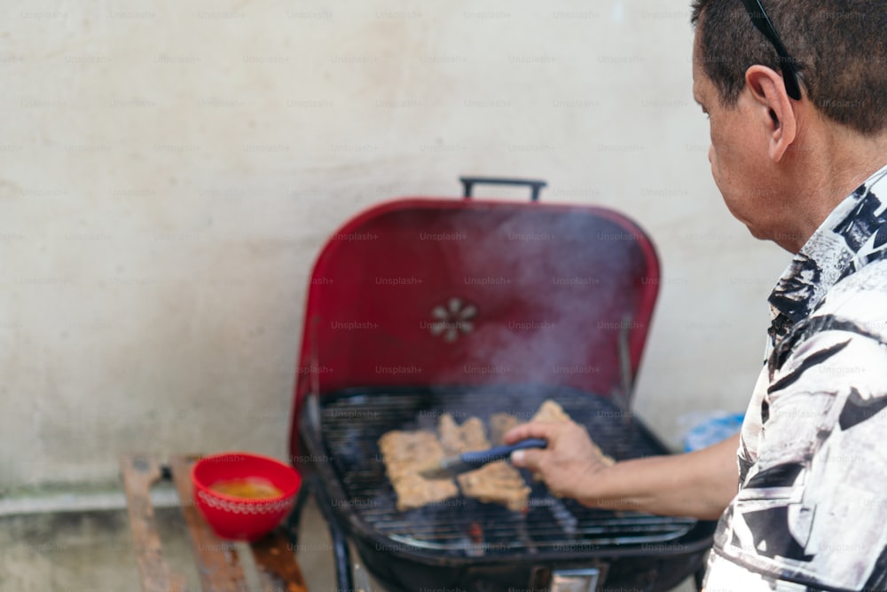 Older man preparing meat on a barbecue grill for his family's lunch in the backyard.