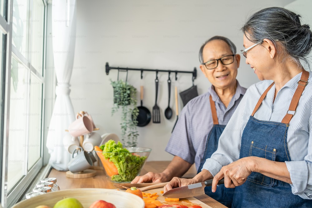 Asian loving senior elderly couple wear apron and cooking in kitchen. Attractive strong old man and woman grandparent wear eyeglass enjoy retirement life activity at home. Family relationship concept.