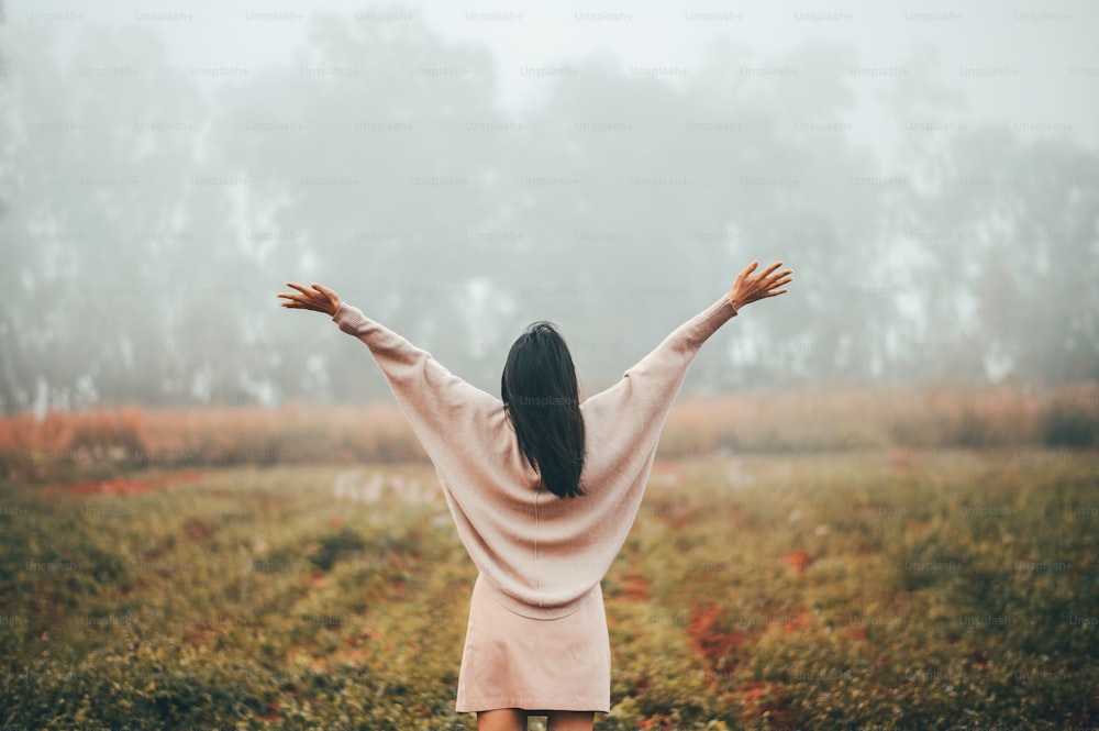 Vista traseira da mulher de braços abertos relaxando e desfrutando da liberdade na névoa da manhã na floresta.