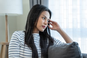 Asian beautiful upset depressed girl sitting alone on bed in bedroom. Attractive unhappy young woman feeling very sad, lonely and upset with life problem then crying with tears in quiet room at house.