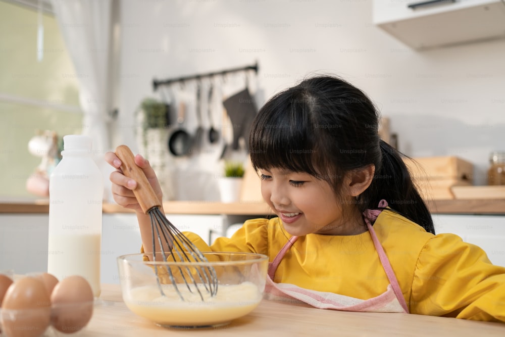 Portrait of Asian young cute kid girl doing homemade bakery in kitchen. Adorable little child sit on table feeling happy and enjoy learn to cooking food or baking  kneads yeast dough with hands at hom