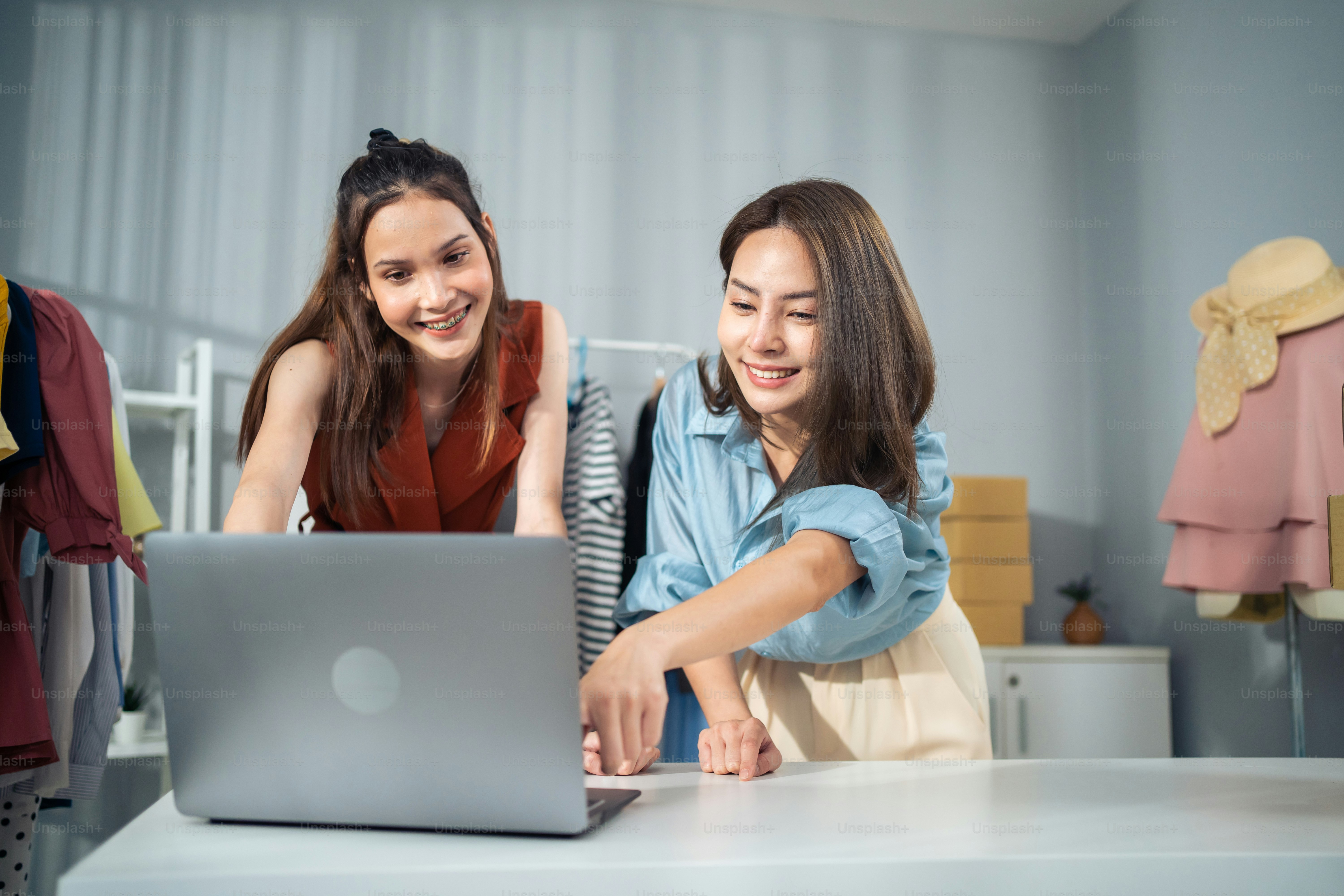 Asian woman friends couple packing clothes order into box for customer. Young attractive business people work to preparing parcel boxes check ecommerce shipping online retail to sell at office store.