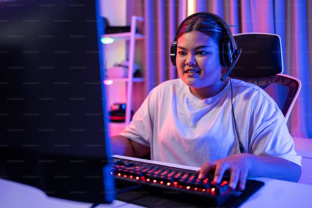 Asiática hermosa mujer jugadora de deportes juega videojuegos en línea en la computadora. La atractiva jugadora de juegos de la joven se siente feliz y disfruta de la transmisión de la tecnología en vivo mientras juega el torneo cibernético en casa