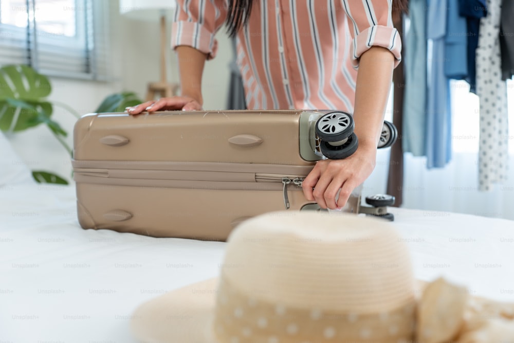 Close up hands of young woman preparing clothes and packing a suitcase. Attractive female tourist traveler feel happy and relax while preparing luggage on bed, ready to travel on holiday vacation trip