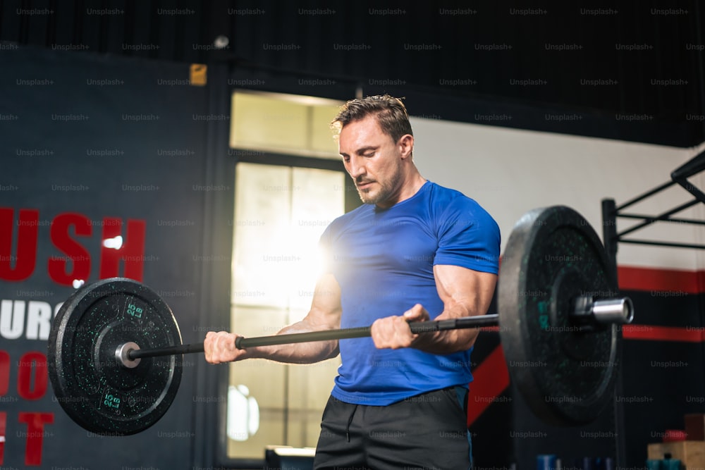 Caucasian sportsman slowly lift up weight machine barbell in stadium. Active fitness trainer or athlete bodybuilder male working out, training exercise to maintain muscle for health care at gym club.