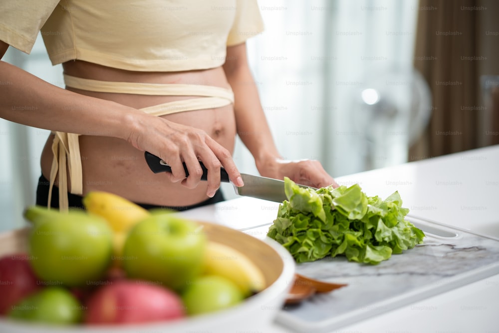 Close up of Asian woman pregnant standing and making vegetable salad. Attractive beautiful young female pregnancy cooking healthy food or vegetarian food in kitchen, Healthy food and pregnancy concept