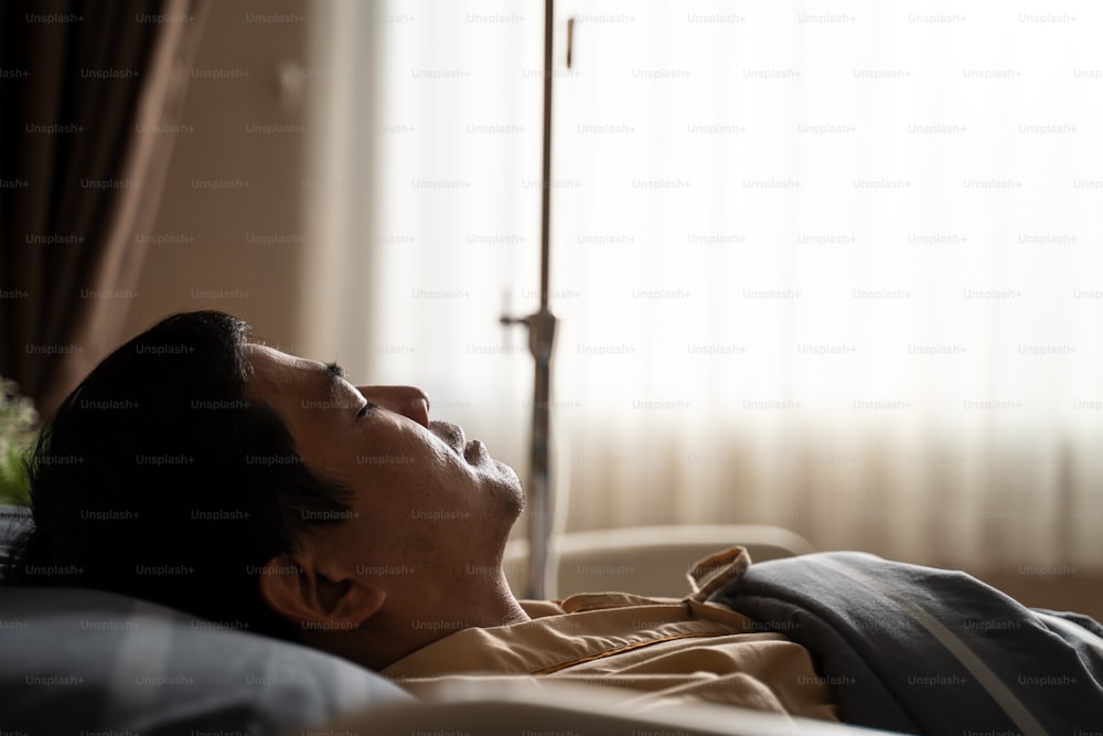 Un patient asiatique inconscient était gravement malade sur son lit dans la salle de réveil de l’hôpital après une intervention chirurgicale dans la salle d’opération. Il dort et se repose pour se remettre d’une maladie. Silhouette lumière de la fenêtre