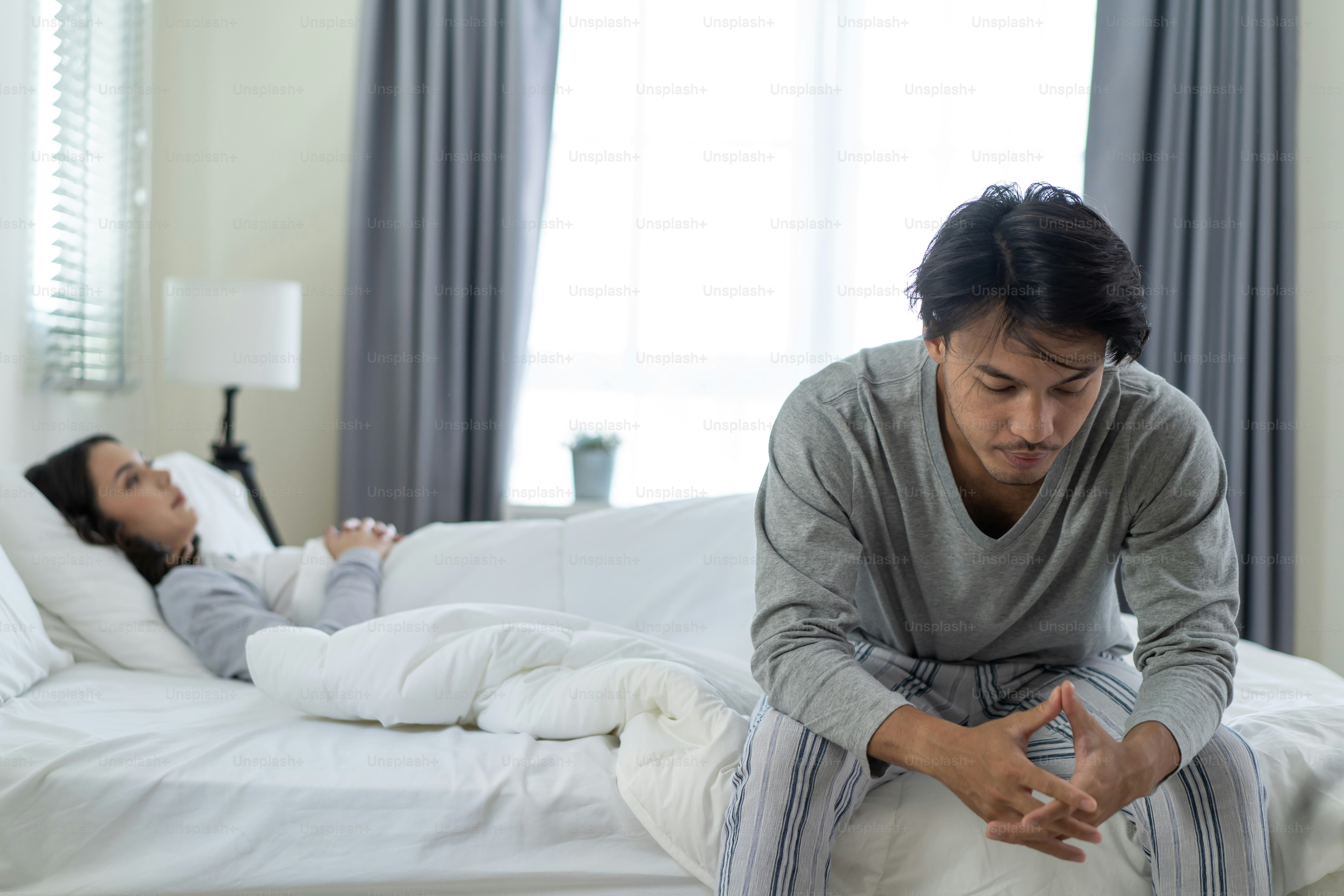 Asian young man feel angry girlfriend having conflict domestic problem. New marriage man and woman feel heartbroken for quarrel conflict while sit on bed in bedroom. Family problem-separation concept.