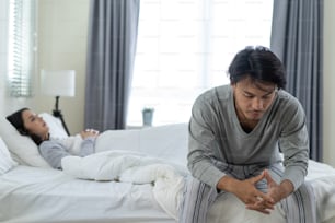 Asiatischer junger Mann fühlt sich wütend Freundin mit Konflikt häuslichen Problem. Neue Ehe Mann und Frau fühlen sich untröstlich für Streit Konflikt, während sie auf dem Bett im Schlafzimmer sitzen. Familienproblem-Trennkonzept.