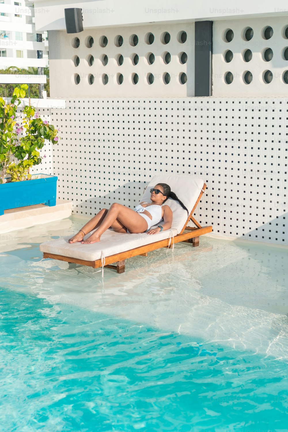 Schönes weibliches Model mit heißem Körper, gesunder Haut in modischer Bademode, Mode-Sonnenbrille, die sich am Pool im Luxusresort entspannt