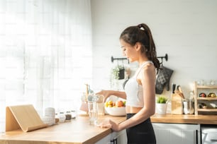 Asian beautiful woman in sportswear drink water after exercise at home. Young thirsty active sport girl takes a sips of clean mineral natural in cup after workout for health care in kitchen in house.